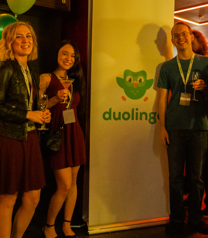 Attendees posing next to a Duolingo roll-up banner